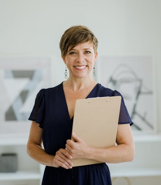 Smiling woman with short hair holding a clipboard in a modern indoor setting.